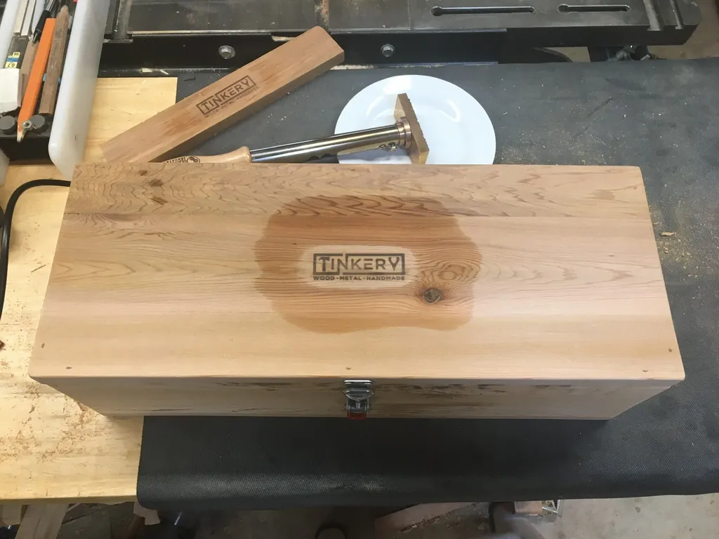 A finished Tinkery-branded wooden box resting on a workbench