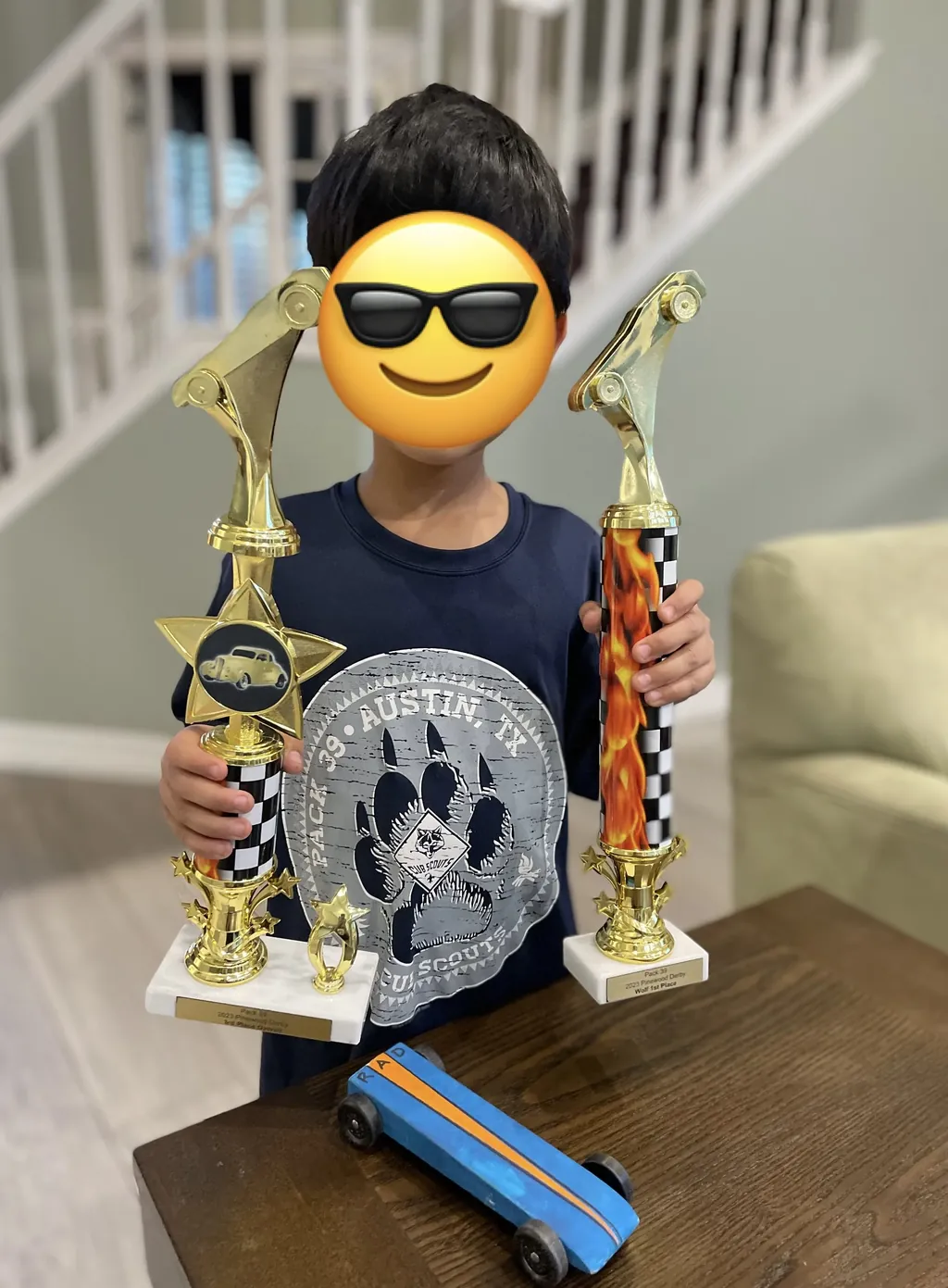 A scout with their pinewood derby car and two trophies